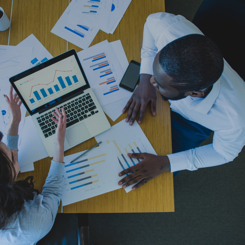 Two colleagues reviewing stock and allocation charts on a laptop spread across a desk.