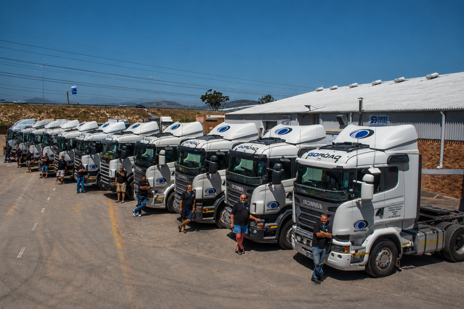 A fleet of GoRoad Scania trucks lined up outside a depot with their drivers standing alongside.