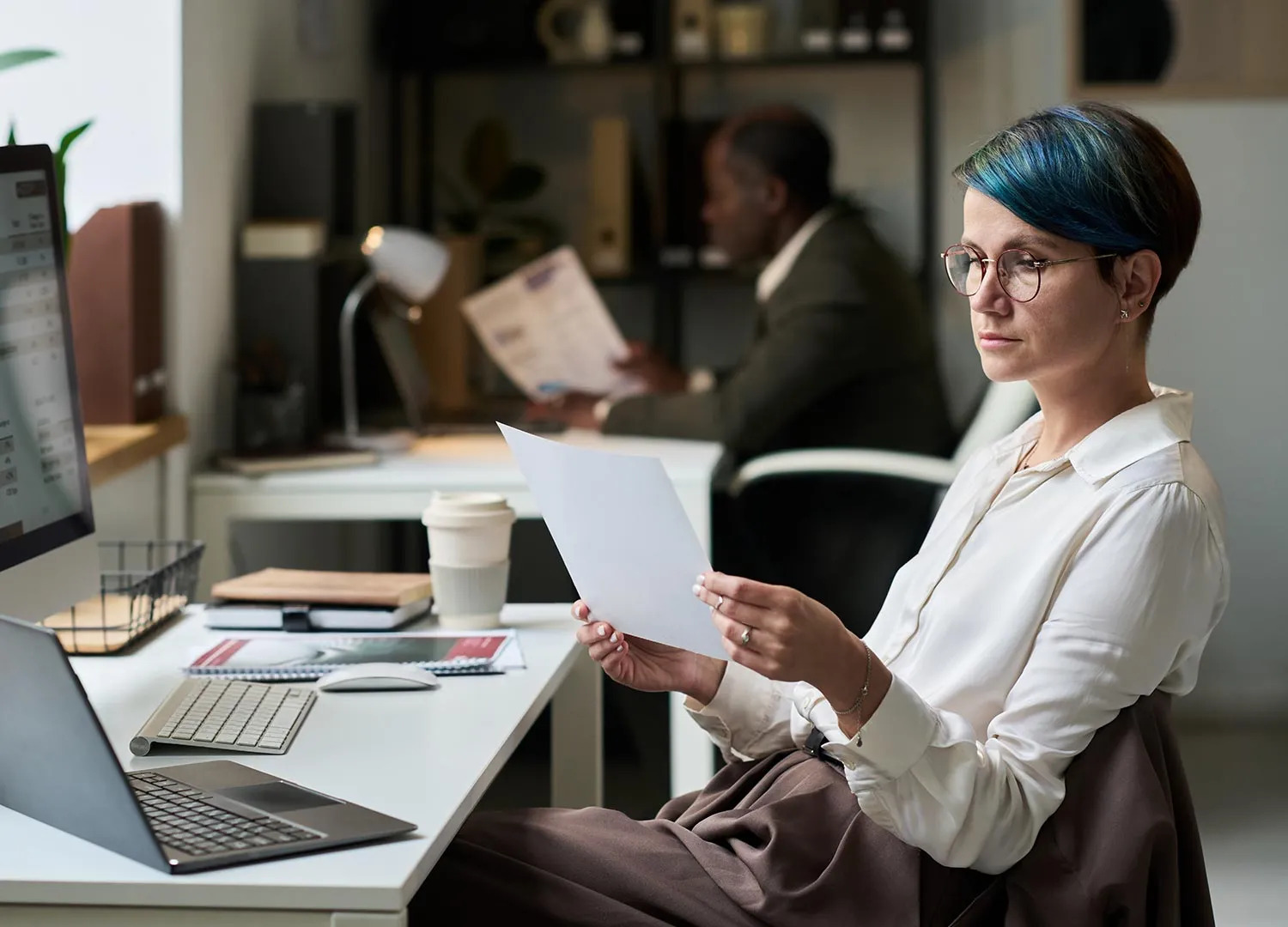 A freight forwarding coordinator reviewing a shipping document at her desk in a busy office.